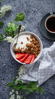 Yoğurtlu gevrek gevrek ve çilek ile fincan sade kahve ve gri arka plan, mükemmel kahvaltı kavramı üzerinde çiçekler ile kase 