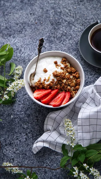 Yoğurtlu gevrek gevrek ve çilek ile fincan sade kahve ve gri arka plan, mükemmel kahvaltı kavramı üzerinde çiçekler ile kase 
