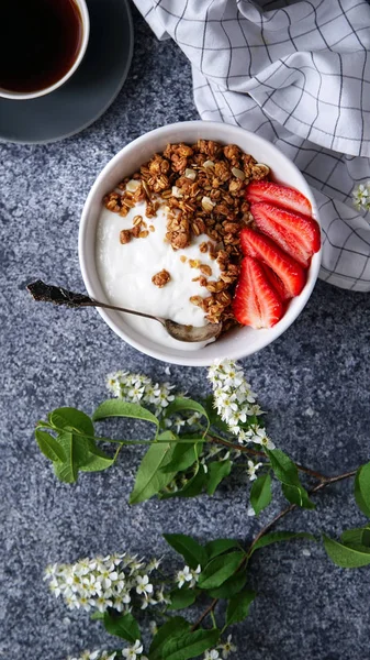 Yoğurtlu gevrek gevrek ve çilek ile fincan sade kahve ve gri arka plan, mükemmel kahvaltı kavramı üzerinde çiçekler ile kase 