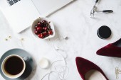 laptop with coffee cup and cherries in bowl with red high-heeled shoes on marble table