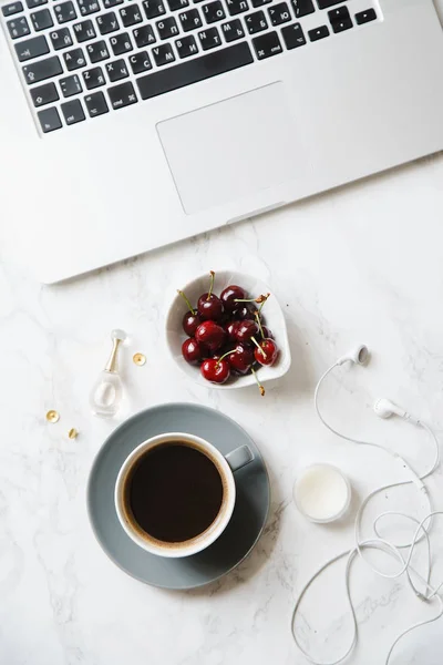 laptop with coffee cup and cherries in bowl on marble table