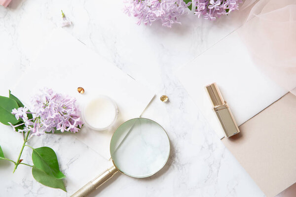 feminine workspace mock-up with lilac flowers and pink accessories on marble background