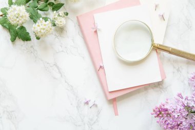 pembe dizüstü ve mermer zemin, kadın blogger çalışma alanı kavramı üzerine altın büyüteç ile beyaz ve Lila çiçek kartlarla 