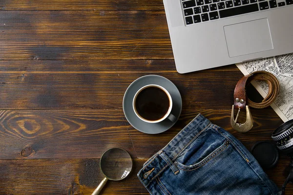 laptop with coffee cup and travel accessories on old vintage wooden table, concept of blogger workspace