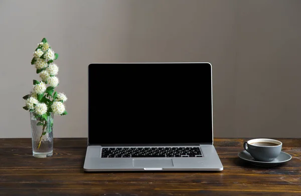 laptop with coffee cup and vase with white flowers on vintage wooden table, concept of blogger workspace