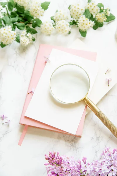 ピンクのノートやカードは大理石の背景 女性ブロガー ワークスペースの概念に黄金の拡大鏡を白と薄紫色の花 — ストック写真