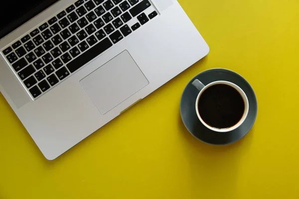 grey opened laptop with hot coffee in cup on bright olive yellow background, concept of female blogger workspace