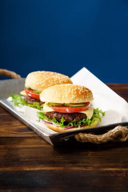 sığır köftesi ile klasik Burger ve domates peynir ve metal tepsi marul ile mavi arka plan karşı ahşap masa servis