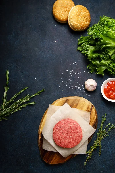 Cutting board with raw patty and buns with rosemary and lettuce on table , concept of cooking burger — Stock Image Cutting Board Raw Patty Buns Rosemary Lettuce Table Concept Cooking Stock Photo