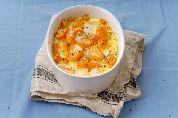bowl with Roasted squash baked and heavy cream with thyme and white wine with parmesan cheese on blue background