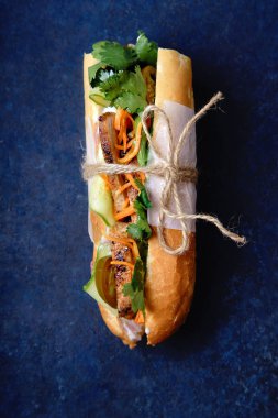 Klasik Banh'da mi sandviç dilimlenmiş ızgara domuz eti bonfile ve soyulmuş salatalık ile rendelenmiş havuç ve koyu mavi zemin üzerine Salantro ile jalapeno biber ile