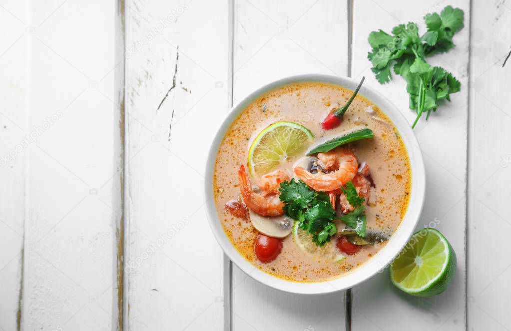 bowl with traditional thai soup tom yum with shrimps and mushrooms served with fresh lime slices on white rustic wooden background