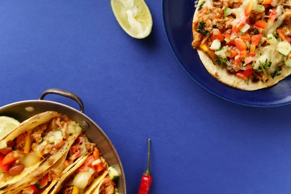 plate and pan with mexican tacos with chili con carne and sweet potatoes with grated cheese served over blue background