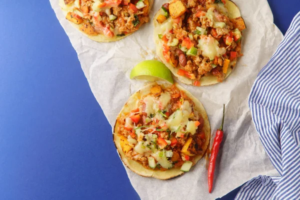 mexican tacos with chili con carne and sweet potatoes with grated cheese served over blue background