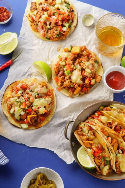 mexican tacos with chili con carne and sweet potatoes with grated cheese served over blue background