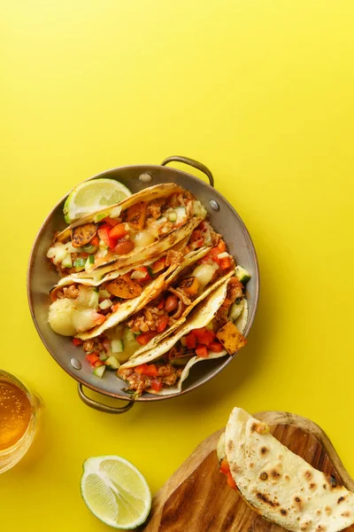 Top view of mexican tacos with chili, sweet potatoes and grated cheese served on blue background