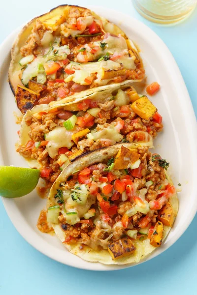 mexican tacos with chili, sweet potatoes and grated cheese served on blue background