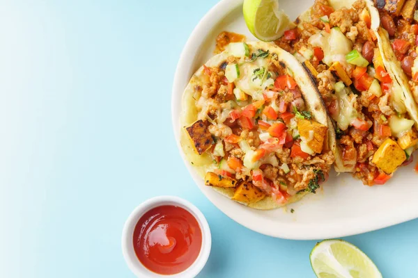 mexican tacos with chili, sweet potatoes and grated cheese served on blue background