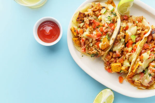 mexican tacos with chili, sweet potatoes and grated cheese served on blue background