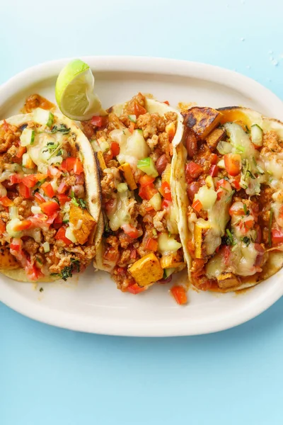 mexican tacos with chili, sweet potatoes and grated cheese served on blue background