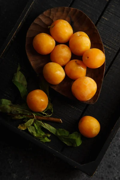 Sweet summer yellow plums with green leaves on wooden tray