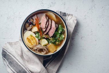 Ramen kavrulmuş Dana, shiitake mantar, kızarmış tofu, pırasa ve keten kumaş beton zemin üzerine yumurta