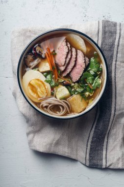 Ramen kavrulmuş Dana, shiitake mantar, kızarmış tofu, pırasa ve keten kumaş beton zemin üzerine yumurta