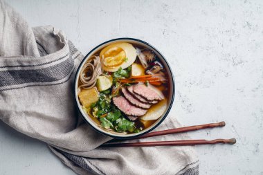 Ramen kavrulmuş Dana, shiitake mantar, kızarmış tofu, pırasa ve keten kumaş beton zemin üzerine yumurta