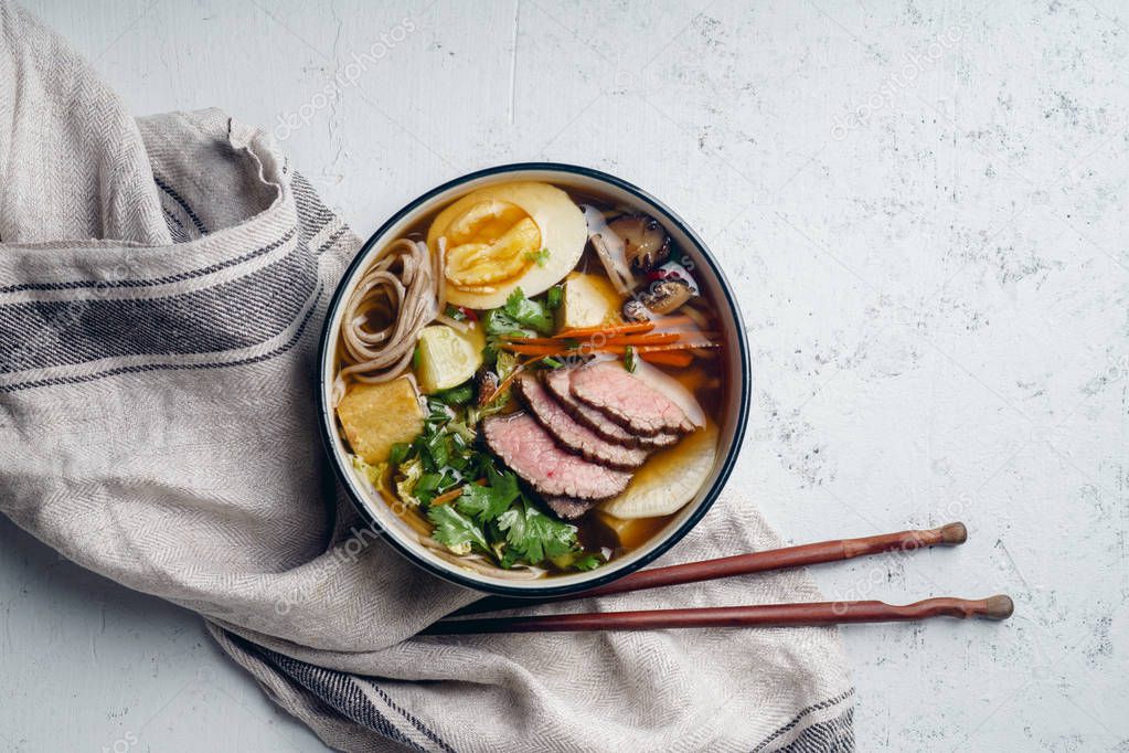 ramen with roasted beef, shiitake mushrooms, fried tofu, leek and eggs on concrete background with linen cloth