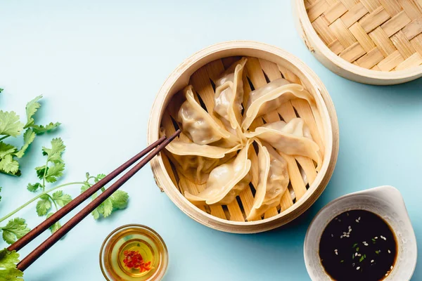 Gyoza dumplings with duck cooked in bamboo steamer served on plate with soy sauce and sesame seeds on blue background, top view