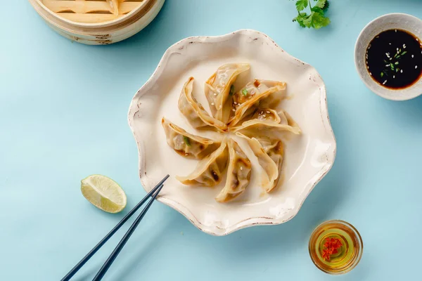 Gyoza dumplings with duck cooked in bamboo steamer served on plate with soy sauce and sesame seeds on blue background, top view