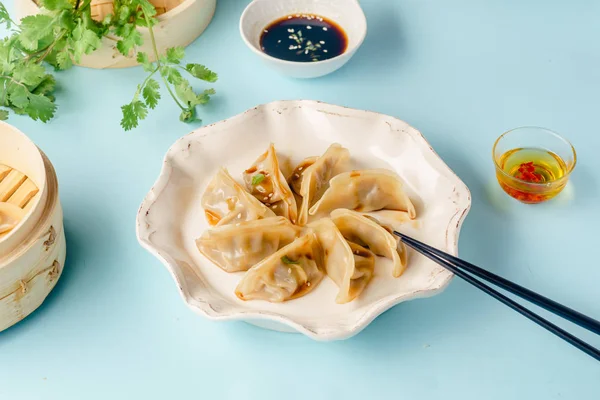 Gyoza dumplings with duck cooked in bamboo steamer served on plate with soy sauce and sesame seeds on blue background, top view