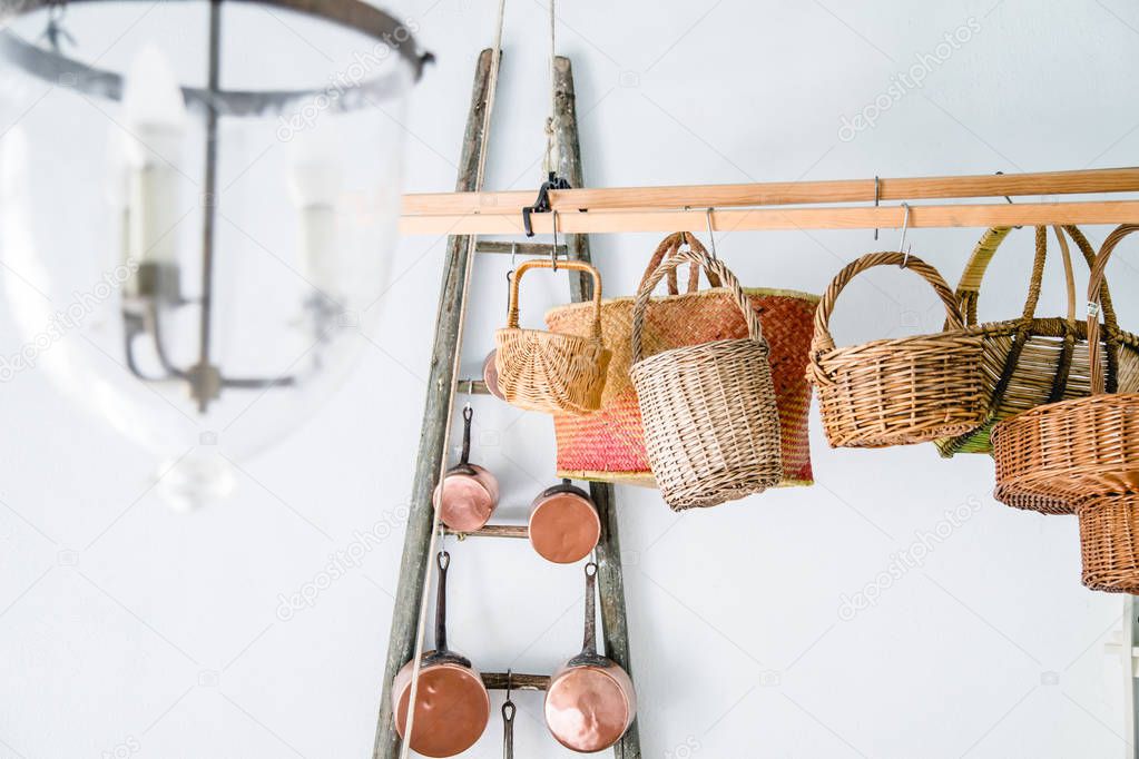 Copper kitchen saucepans and baskets hanging on racks near white wall
