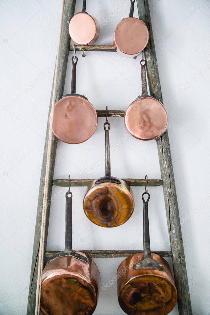 Copper kitchen saucepans hanging on rack near white wall