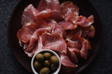 Ahşap plaka üzerinde ince Jambon dilimleri karanlık beton zemin üzerine yeşil zeytin ile