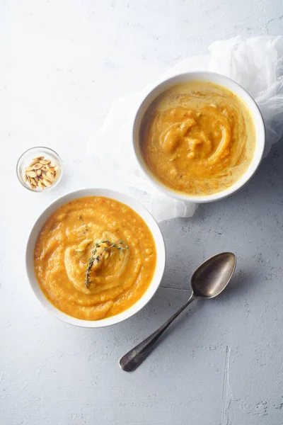 Pureed pumpkin soup with seeds and thyme in bowls on concrete background. Warm food concept, dieting