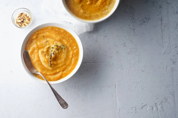 Pureed pumpkin soup with seeds and thyme in bowls on concrete background. Warm food concept, dieting