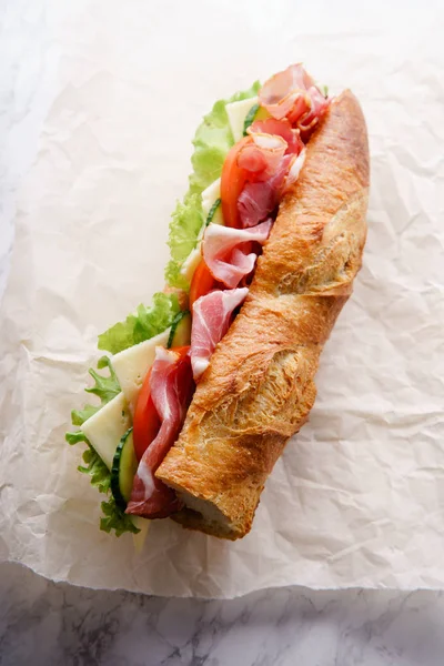 wrapping paper with fresh baguette sandwich banh-mi styled on white marble background