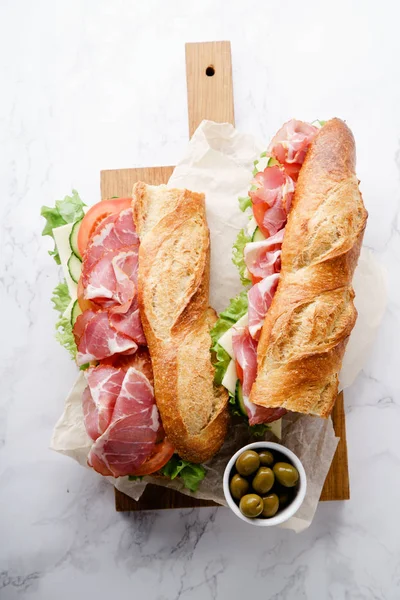 Fresh baguette sandwiches banh-mi styled with ham and tomatoes with fresh lettuce on wooden cutting board