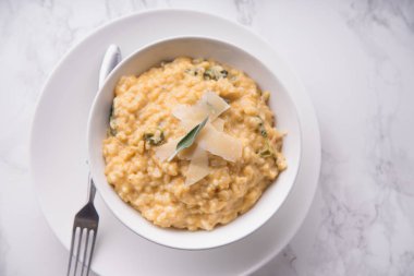 Kabak risotto ile parmesan ve beyaz mermer zemin üzerinde adaçayı