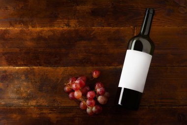 Şarap şişesi ve ahşap arka plan, üstten görünüm üzerinde kırmızı üzüm ile düz yatıyordu mockup 