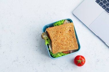 Dizüstü yakınındaki plastik kap içinde Yeşiller ve jambon ile sağlıklı sandviç Paketli. İş yerinde öğle yemeği için paket servisi olan restoran gıda 