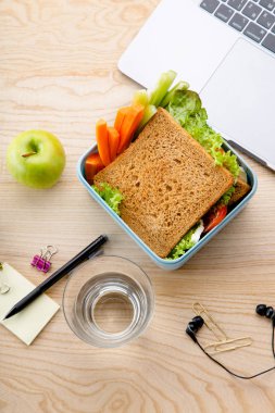 sağlıklı sandviç meyveleri ve office öğeleri ahşap masa üzerinde açılan dizüstü yanında plastik kap içinde. İş yerinde öğle yemeği için paket servisi olan restoran gıda 