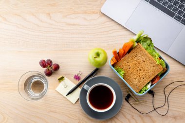 sağlıklı sandviç meyveleri ve office öğeleri ahşap masa üzerinde açılan dizüstü yanında plastik kap içinde. İş yerinde öğle yemeği için paket servisi olan restoran gıda 