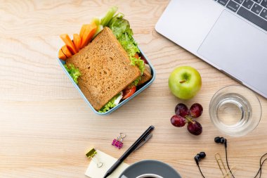 sağlıklı sandviç meyveleri ve office öğeleri ahşap masa üzerinde açılan dizüstü yanında plastik kap içinde. İş yerinde öğle yemeği için paket servisi olan restoran gıda 