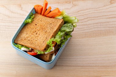 Yeşiller ve sebze ahşap arka plan üzerinde plastik kapta jambon ile sağlıklı sandviç. Ofis öğle yemeği kavramı