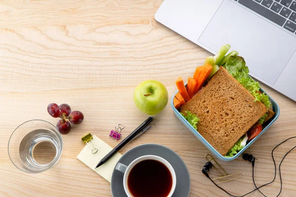 sağlıklı sandviç meyveleri ve office öğeleri ahşap masa üzerinde açılan dizüstü yanında plastik kap içinde. İş yerinde öğle yemeği için paket servisi olan restoran gıda 