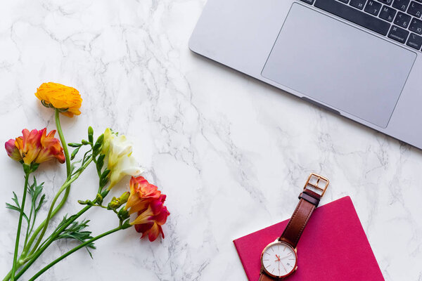 laptop with fresh freesia flowers and watch on marble background