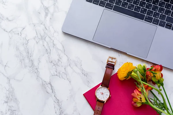 laptop with fresh freesia flowers and watch on marble background