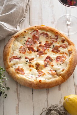 Beyaz ahşap sıkıntılı masada şarap kadehi ile servis domuz pastırması ve kekik ile peynir ile pişmiş pizza üst görünümü